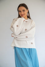 Load image into Gallery viewer, Woman wearing a white sweater with heart patterns and a blue skirt against a plain background