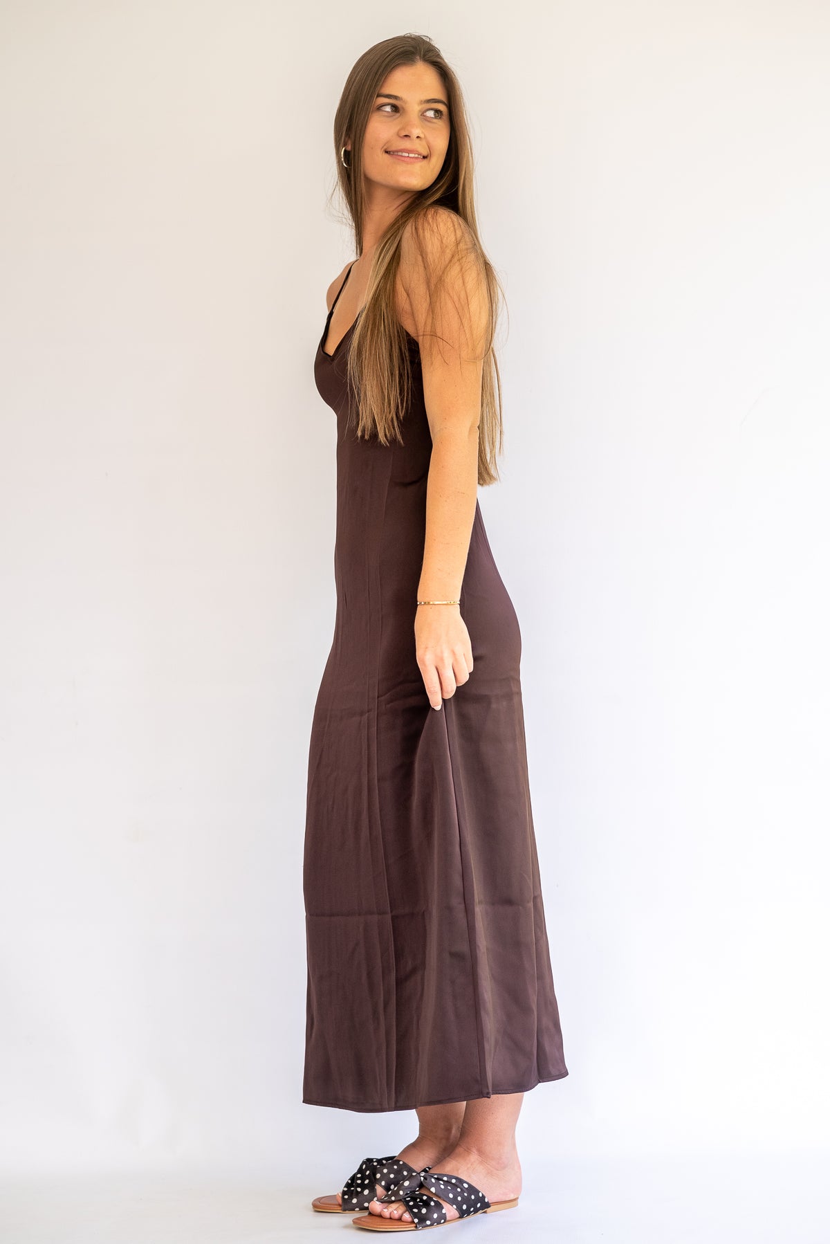 Woman wearing a chocolate brown satin dress against a white background
