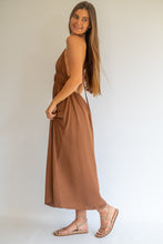 Load image into Gallery viewer, A woman modeling a sleeveless, brown maxi dress with a side cutout, paired with strappy flat sandals, photographed against a plain white studio background.
